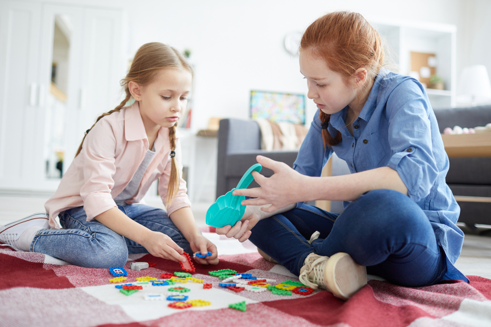Full,Length,Portrait,Of,Two,Sisters,Playing,With,Puzzles,Sitting